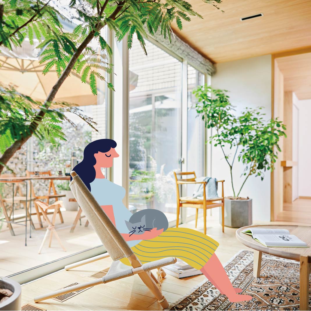 窓際のリビングで椅子に座り猫を膝に乗せてくつろぐ女性の画像